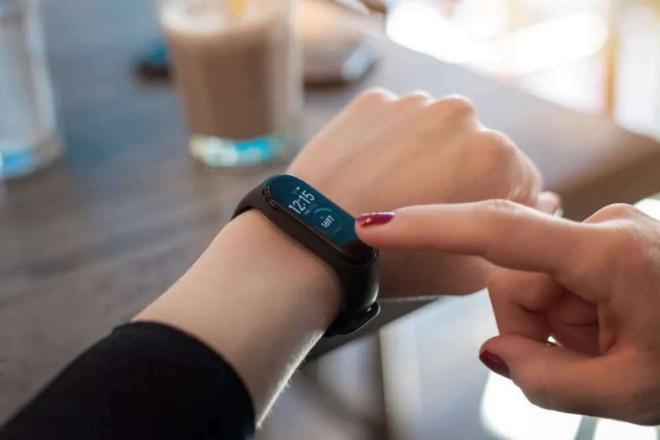Close-up of wrist with smart watch and other hand reaching for display.